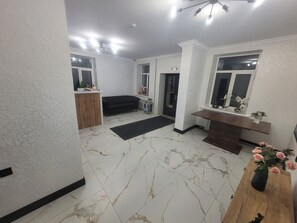 A living room with a marble floor, a black sofa, a wooden coffee table, and a window with flowers.