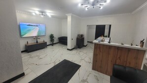 Un espace d’accueil moderne avec un sol en marbre, un téléviseur à écran plat, un comptoir de réception et un canapé en cuir noir.