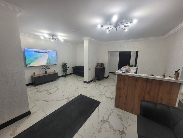 A modern reception area with a marble floor, a flat-screen TV, a reception desk, and a black leather sofa.