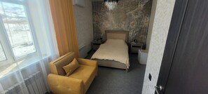 A bedroom with a bed, a sofa, a nightstand, a dresser, and a window with curtains.