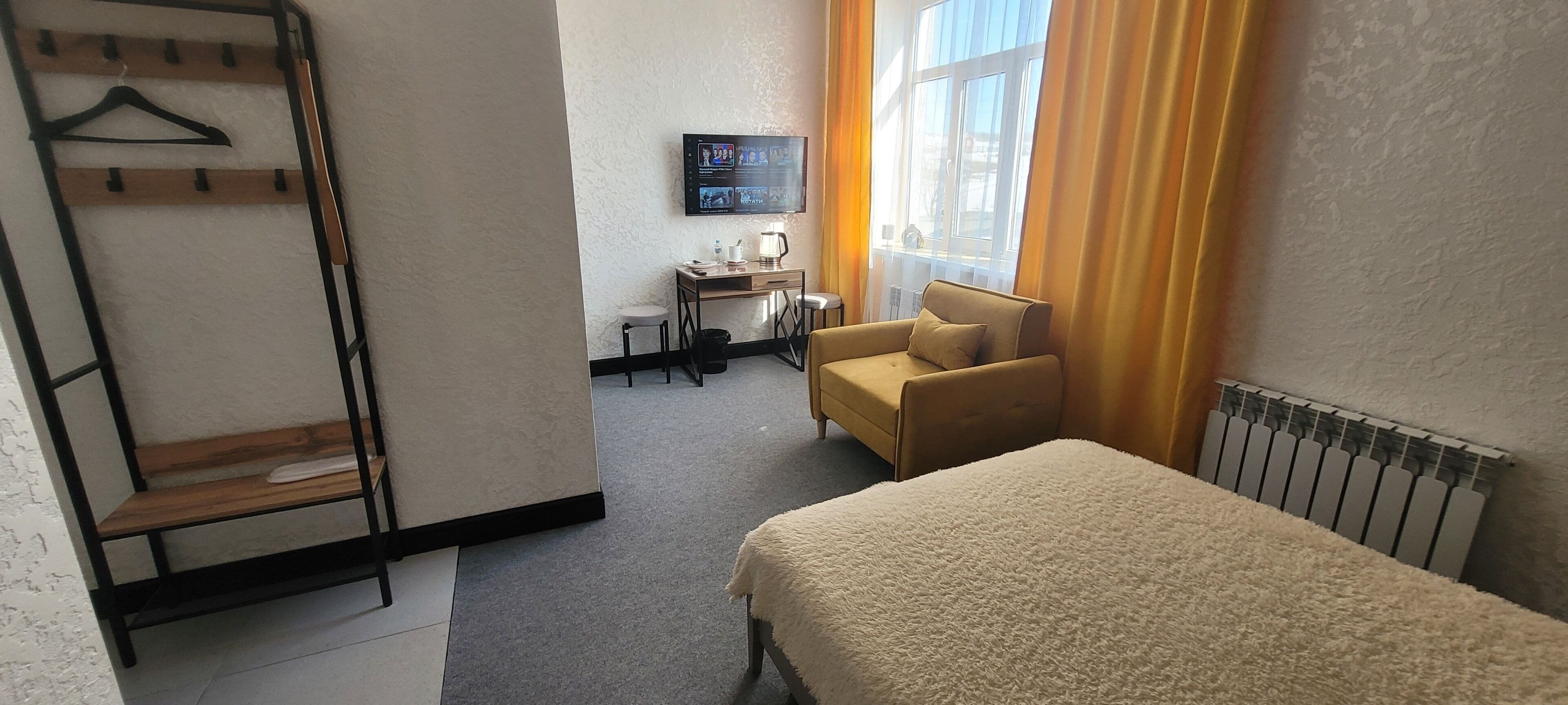 Una habitación de hotel con una cama, un escritorio con silla, un televisor y un radiador.