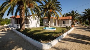 A two-story building with a white facade, a red-tiled roof, and a central fountain.