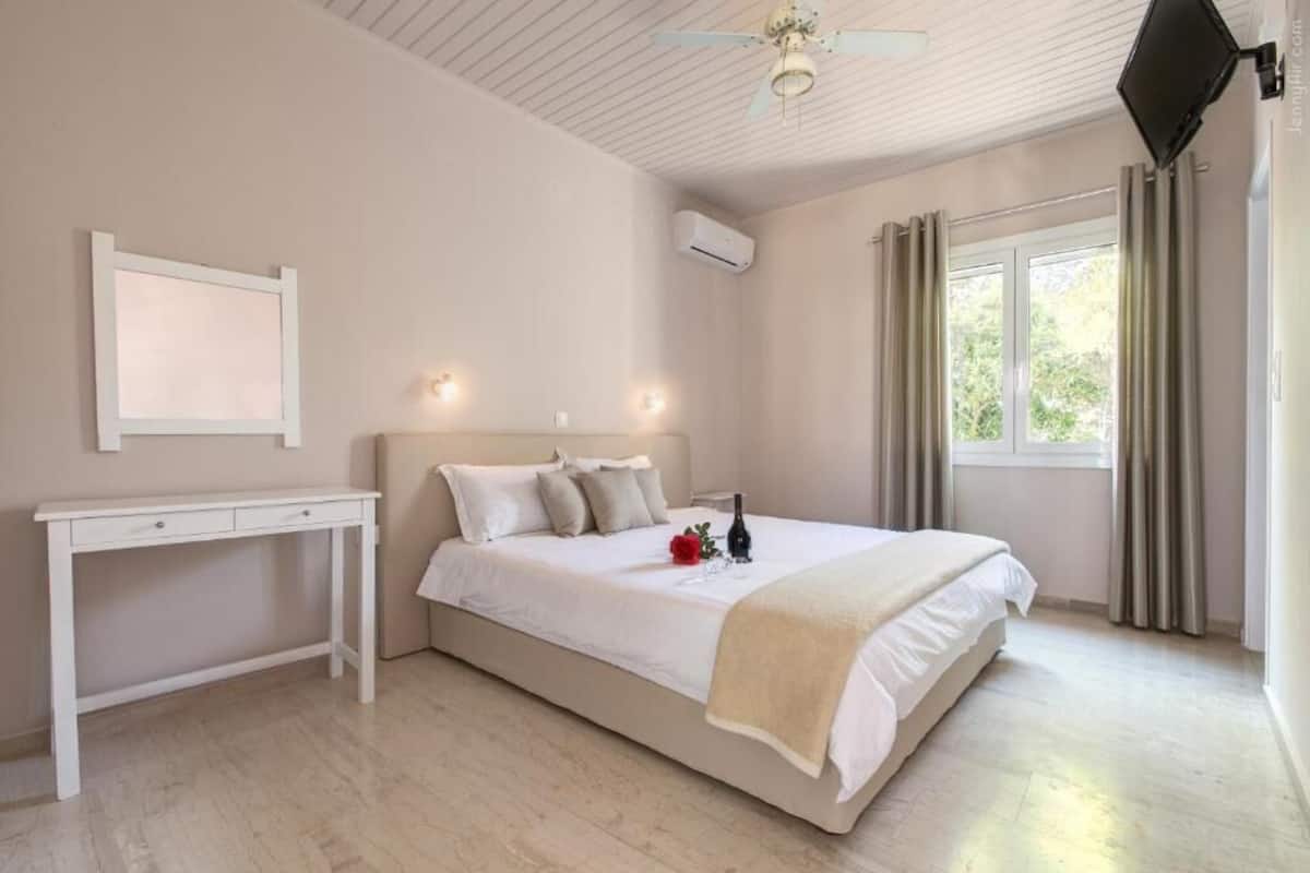 A bedroom with a bed, a desk, a ceiling fan, an air conditioning unit, and a window with curtains.