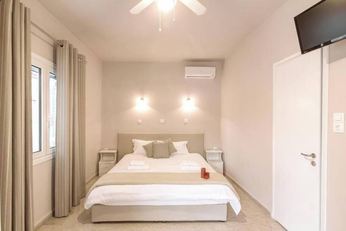 A hotel room with a bed, bedside tables, a ceiling fan, an air conditioning unit, and a television.