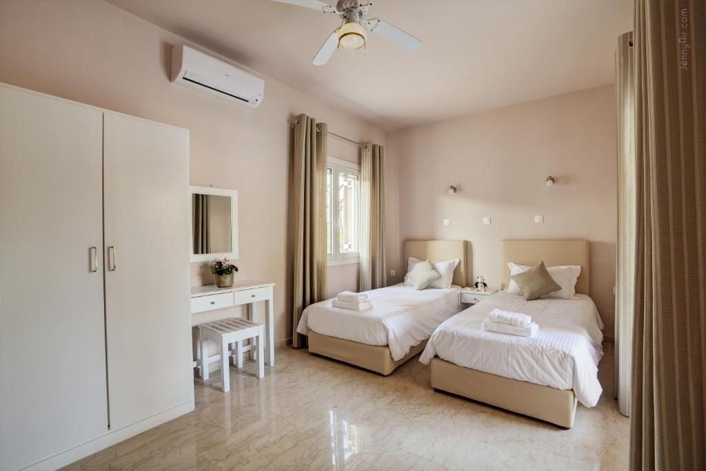 A hotel room with two beds, a desk, a chair, a ceiling fan, and an air conditioning unit.