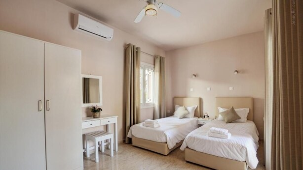 A hotel room with two beds, a desk, a chair, a ceiling fan, and an air conditioning unit.