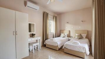 A hotel room with two beds, a desk, a chair, a ceiling fan, and an air conditioning unit.