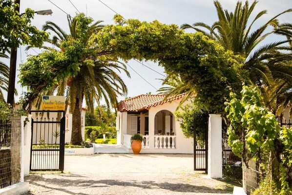 A gated entrance to a building with a tiled roof, surrounded by lush greenery and palm trees.
