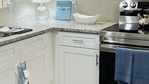Una cocina con armarios blancos, estufa de acero inoxidable, microondas y un tapete azul.