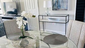 Una sala moderna con una mesa de centro de vidrio, dos sillones, un jarrón con orquídeas blancas, una obra de arte enmarcada y una consola minimalista.