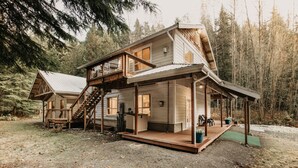 A two-story cabin with a deck, surrounded by forest. - Welcome to The Baker House Retreat - The Ranch House and The Bunk House (Maple Falls)