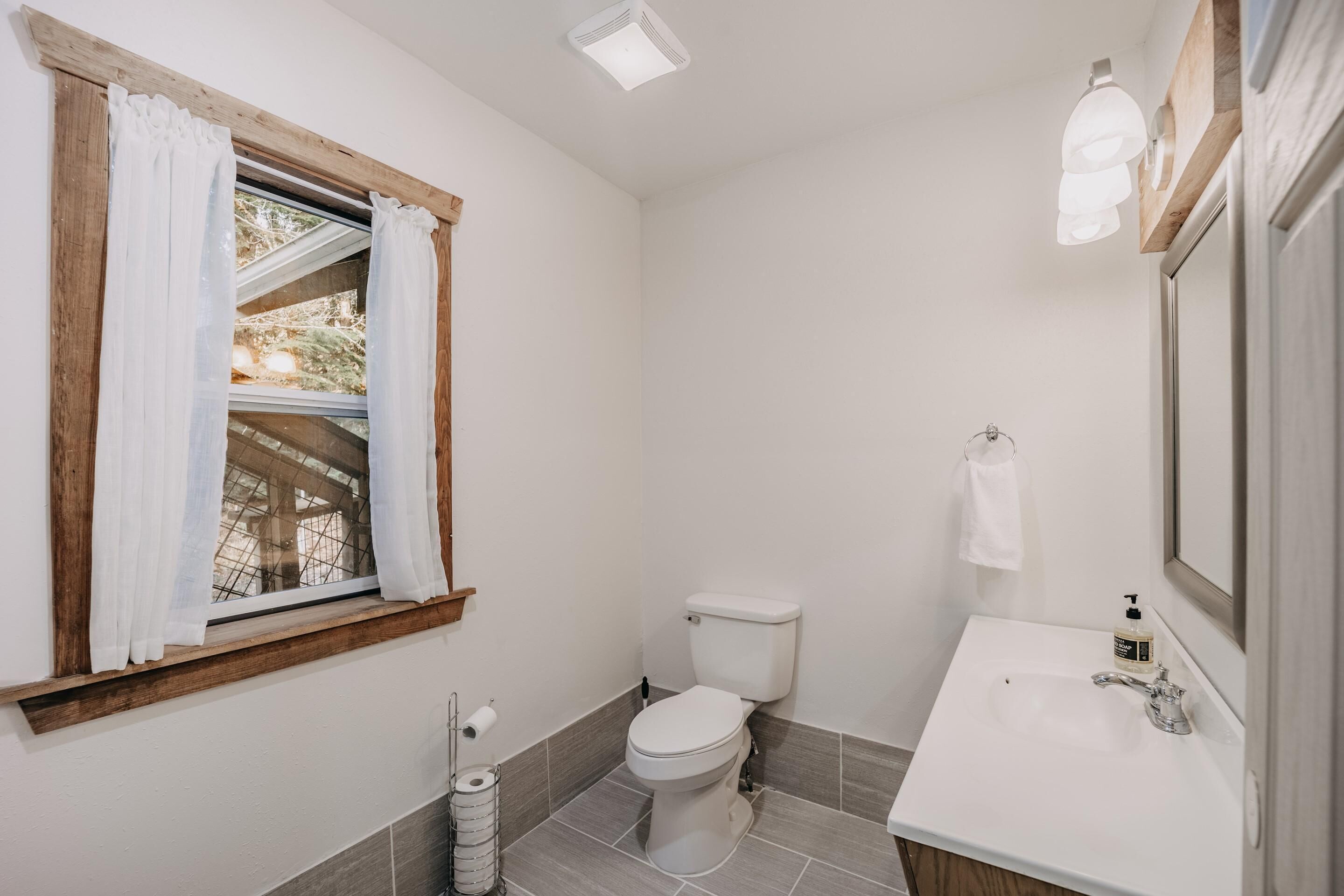 A bathroom with a toilet, sink, and window with curtains.
