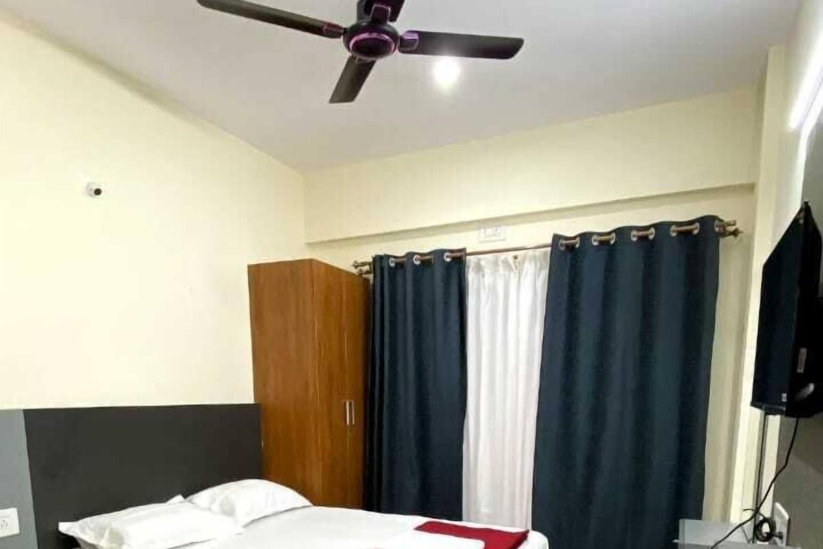 A hotel room with two beds, a ceiling fan, a wardrobe, a desk with a chair, and a television.