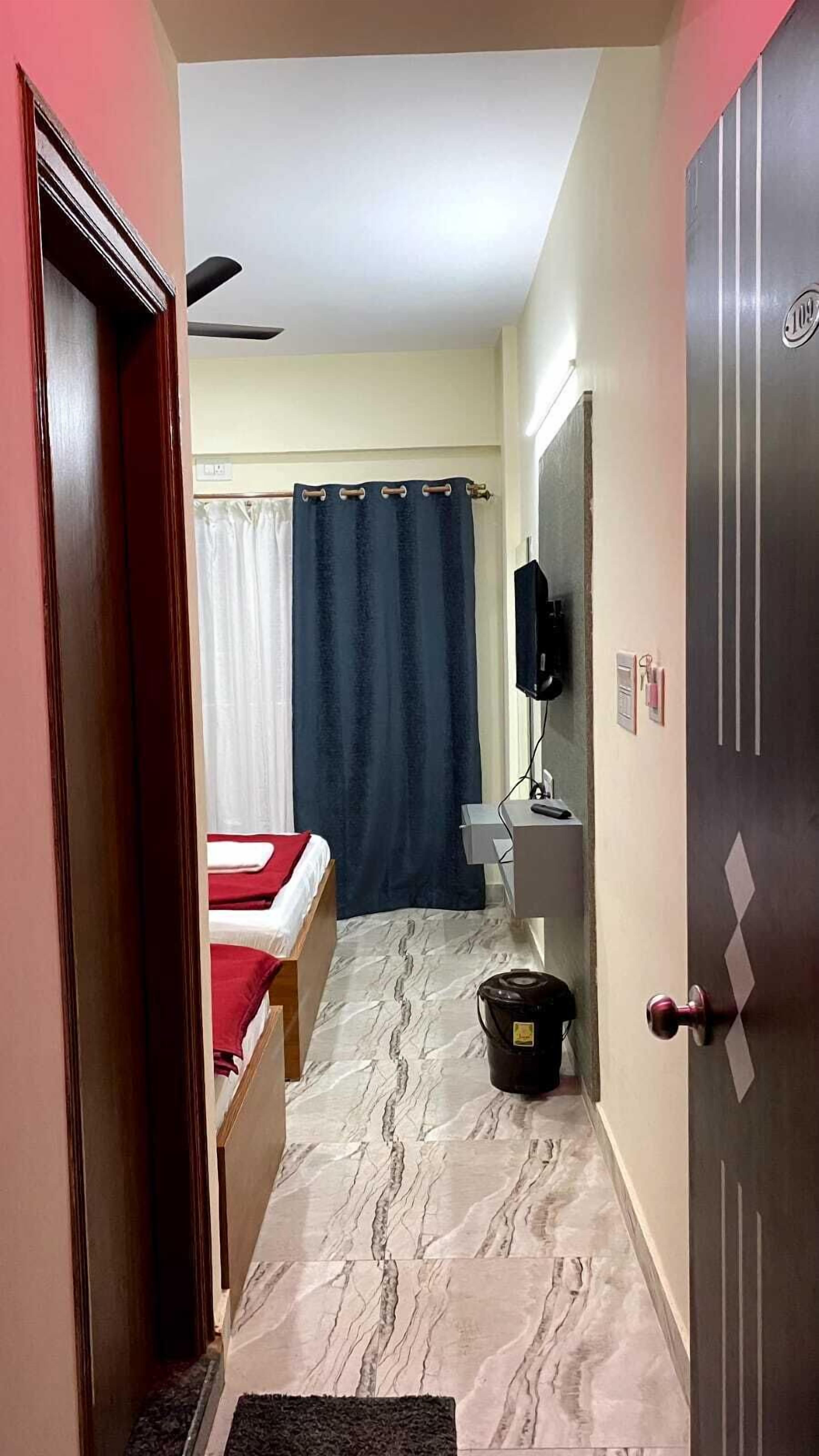 A narrow hallway with a bed, a toilet, and a television mounted on the wall.