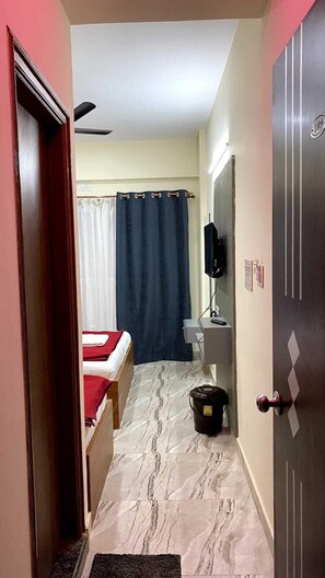 A narrow hallway with a bed, a toilet, and a television mounted on the wall. - HKP Residency (Bengaluru)