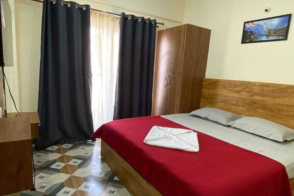 A hotel room with a bed, a wooden wardrobe, a desk, and a window with curtains.