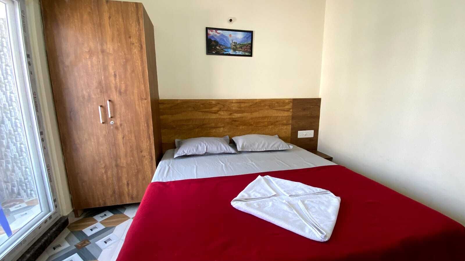 Camera d'albergo con un letto, un armadio in legno, un quadro appeso al muro e una finestra.