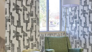 A room with patterned wallpaper, a large window, and a green armchair. - Lititz Pointe Inn and Suites (Lititz)