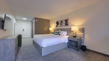 A hotel room with a bed, bedside tables, a desk, a chair, a wardrobe, and a TV.