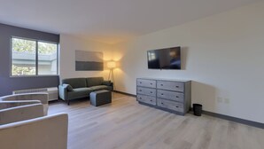 A modern living room with a grey sofa, a small ottoman, a grey dresser, and a flat-screen TV on the wall. - Lititz Pointe Inn and Suites (Lititz)