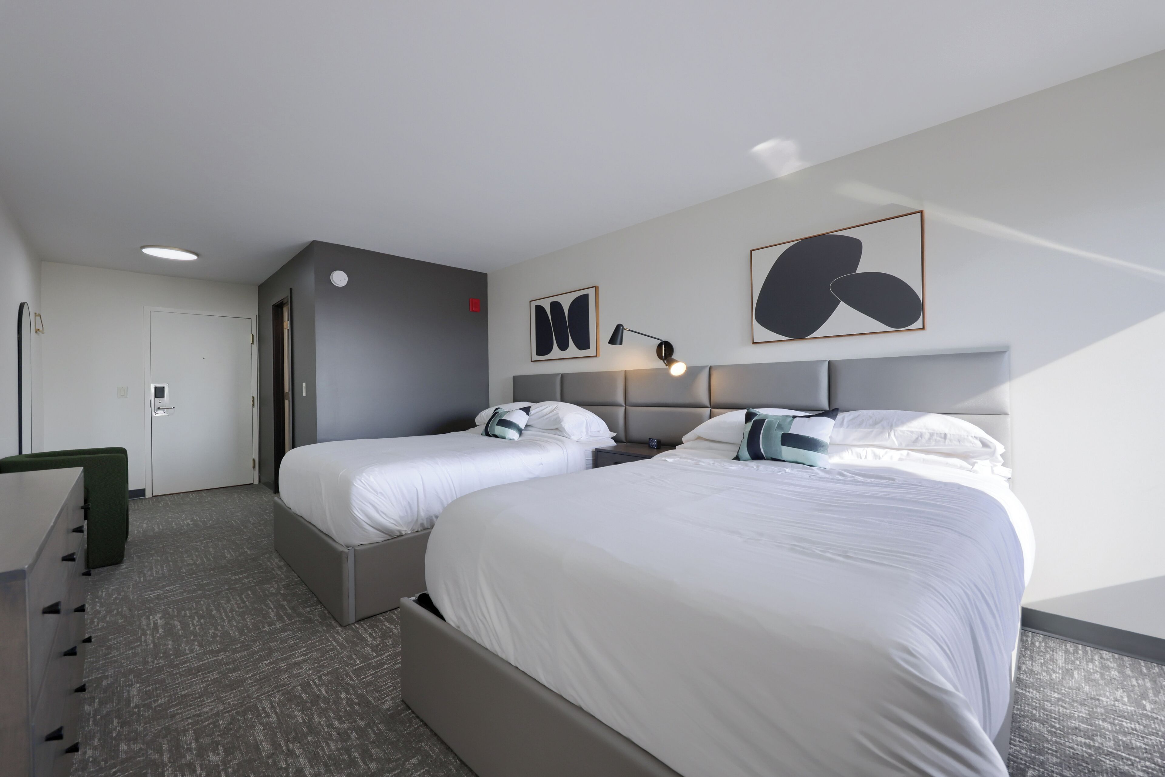 Quarto de hotel com duas camas, uma escrivaninha, uma cadeira e um guarda-roupa.