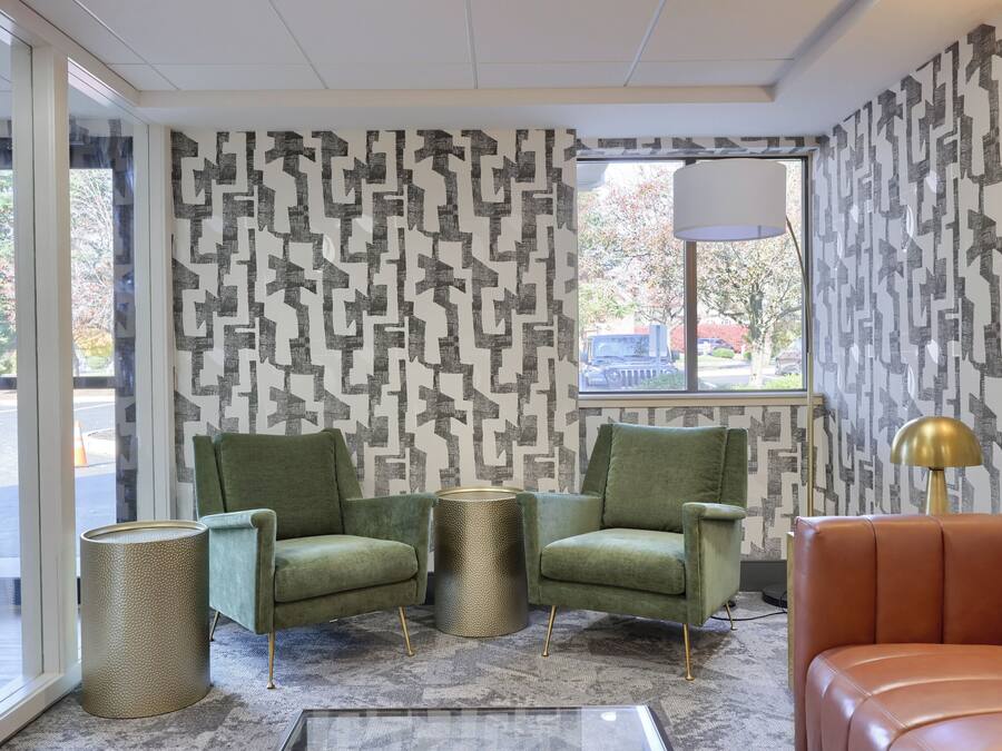 A modern living room with patterned wallpaper, green armchairs, a round side table, and a leather sofa.