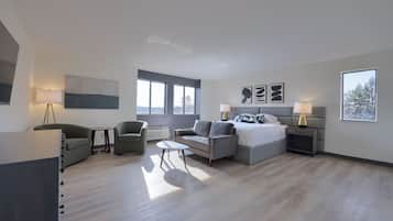 Habitación de hotel moderna con cama, dos sillones, una mesita y un escritorio. Amplias ventanas ofrecen luz natural y vistas al exterior.