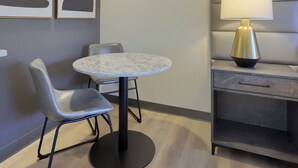 A modern room with a round marble table, two grey upholstered chairs, a wall-mounted lamp, and abstract artwork. - Lititz Pointe Inn and Suites (Lititz)