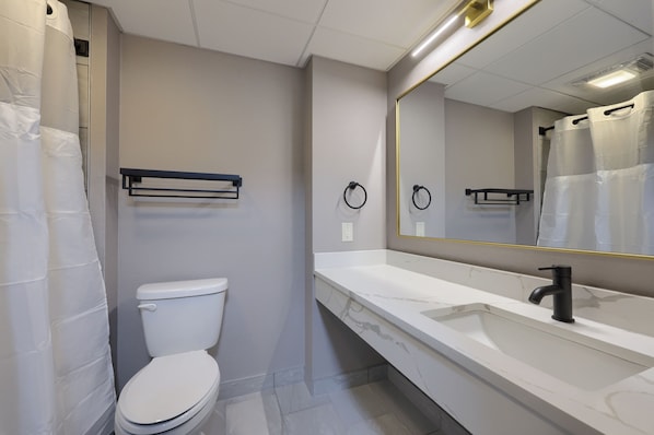 Un baño moderno con inodoro blanco, un espejo grande y lavamanos blanco.