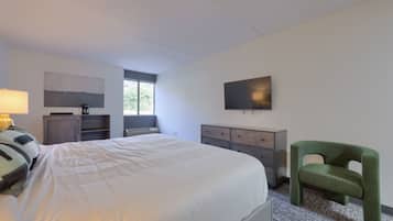 A modern hotel room with a large bed, a desk, a chair, a TV, and a window.