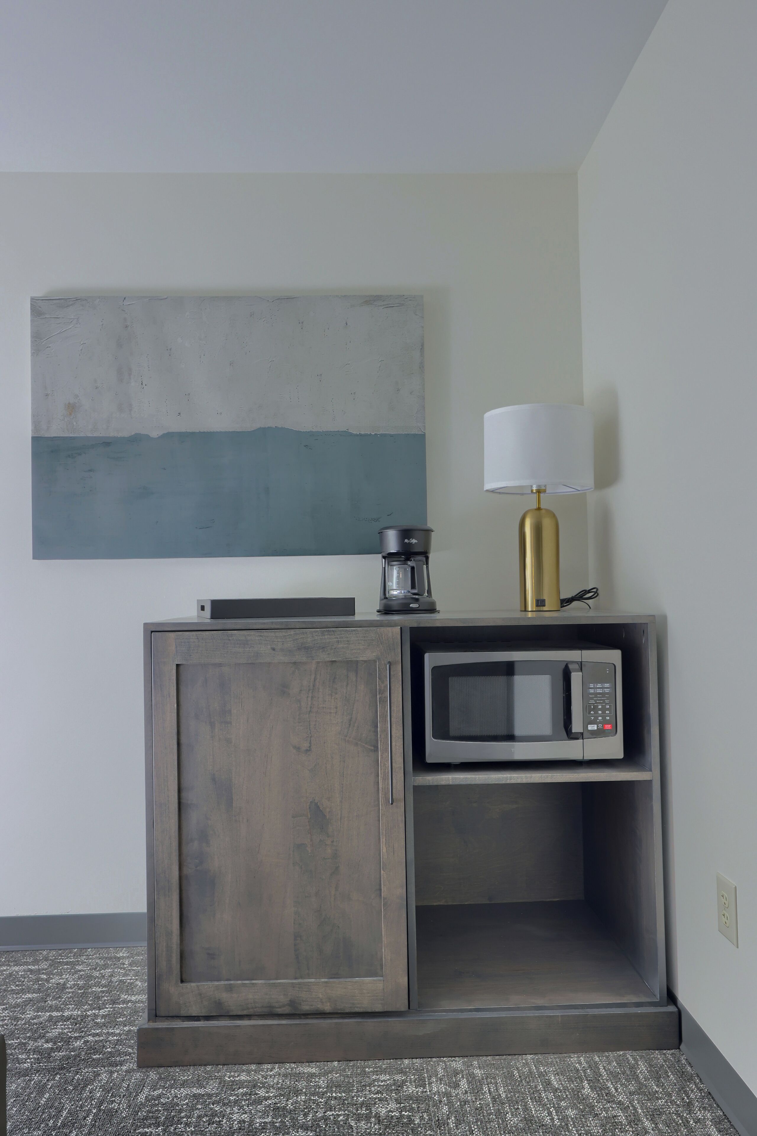 A kitchenette with a microwave, coffee maker, and a lamp on a cabinet.