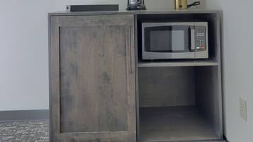 A kitchenette with a microwave, coffee maker, and a lamp on a cabinet.