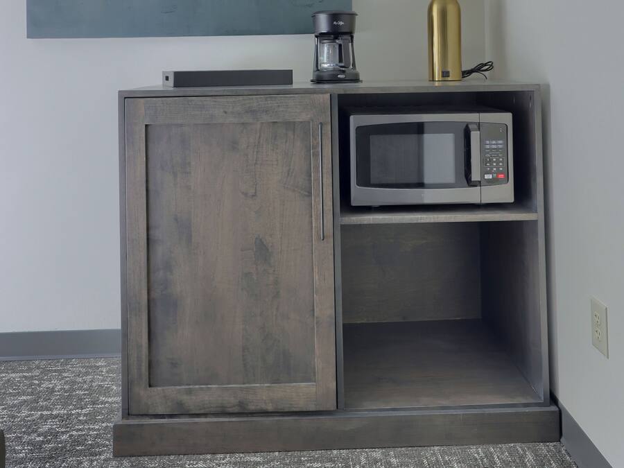 A kitchenette with a microwave, coffee maker, and a lamp on a cabinet.
