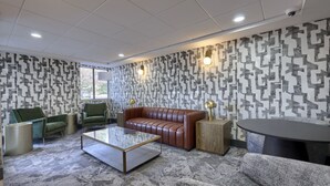 A modern lounge area with a brown leather sofa, green armchairs, a glass coffee table, and patterned wallpaper. - Lititz Pointe Inn and Suites (Lititz)