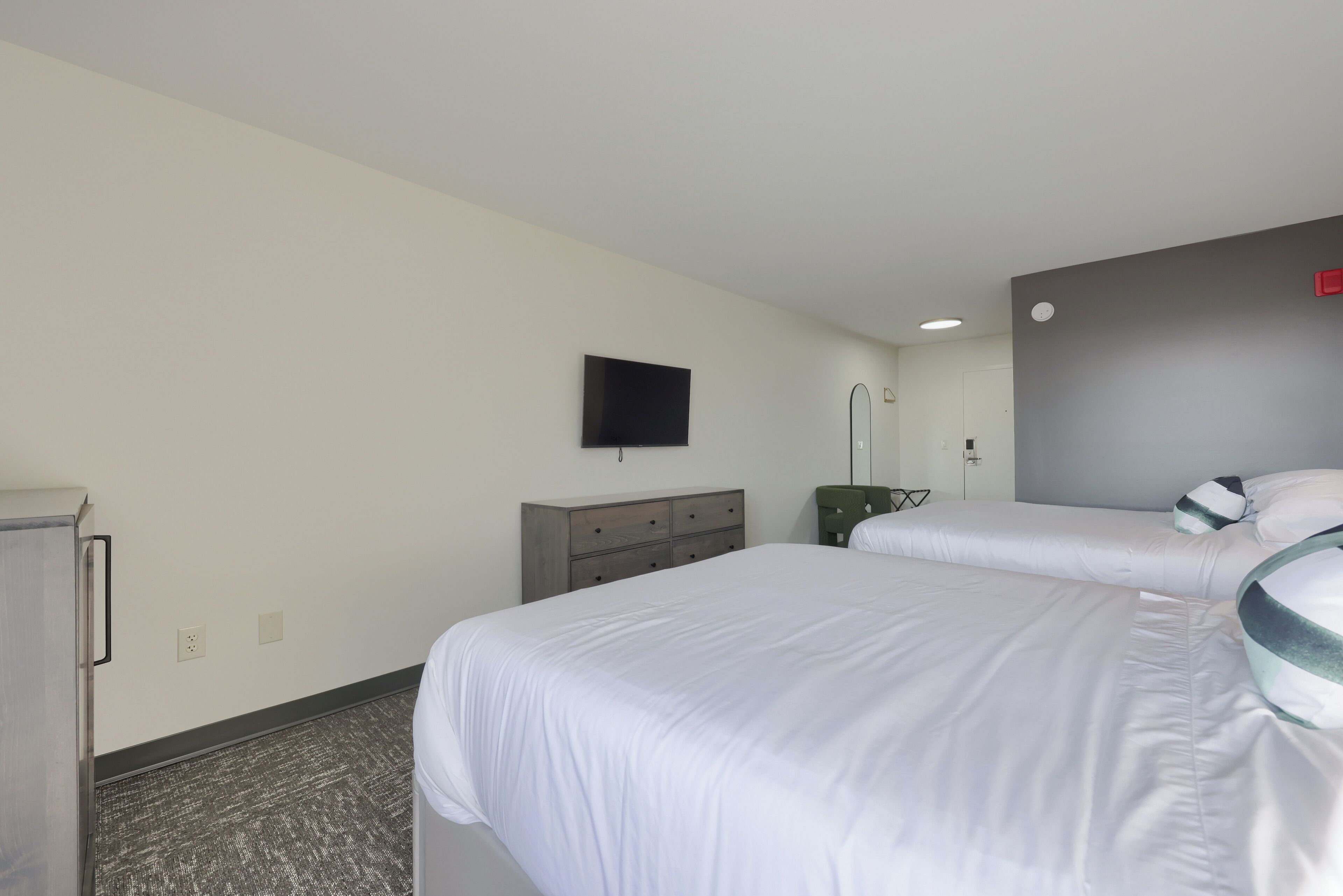 Una habitación de hotel con dos camas, un televisor de pantalla plana montado en la pared, un aparador y un espejo.