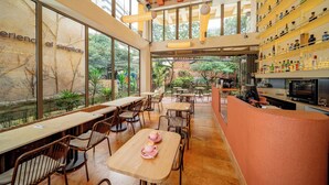 A spacious café with large windows, wooden tables, and chairs, and a bar area with shelves of bottles. - Moabi Hotel (Medellín)