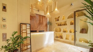 A reception area with a wooden reception desk, a large mirror, and a wall with shelves displaying decorative items. - Moabi Hotel (Medellín)