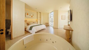 A spacious bedroom with a large bathtub, a bed with a green blanket, and a chair. - Moabi Hotel (Medellín)