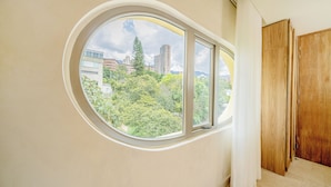 A room with a large circular window offering a view of a cityscape and greenery. - Moabi Hotel (Medellín)