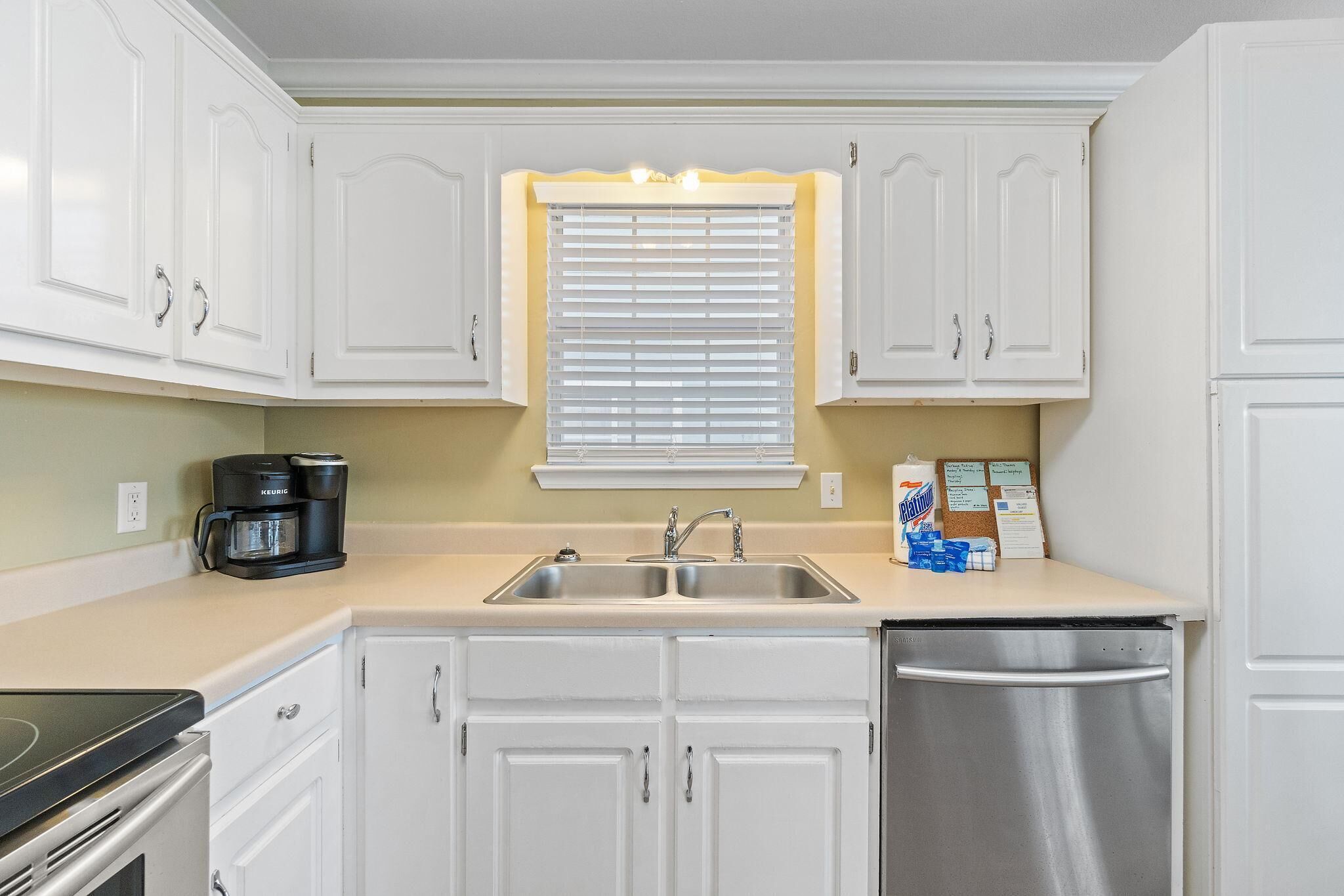 A compact kitchen with white cabinets, a double sink, a coffee maker, and a dishwasher.