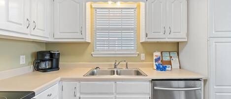 A compact kitchen with white cabinets, a double sink, a coffee maker, and a dishwasher.