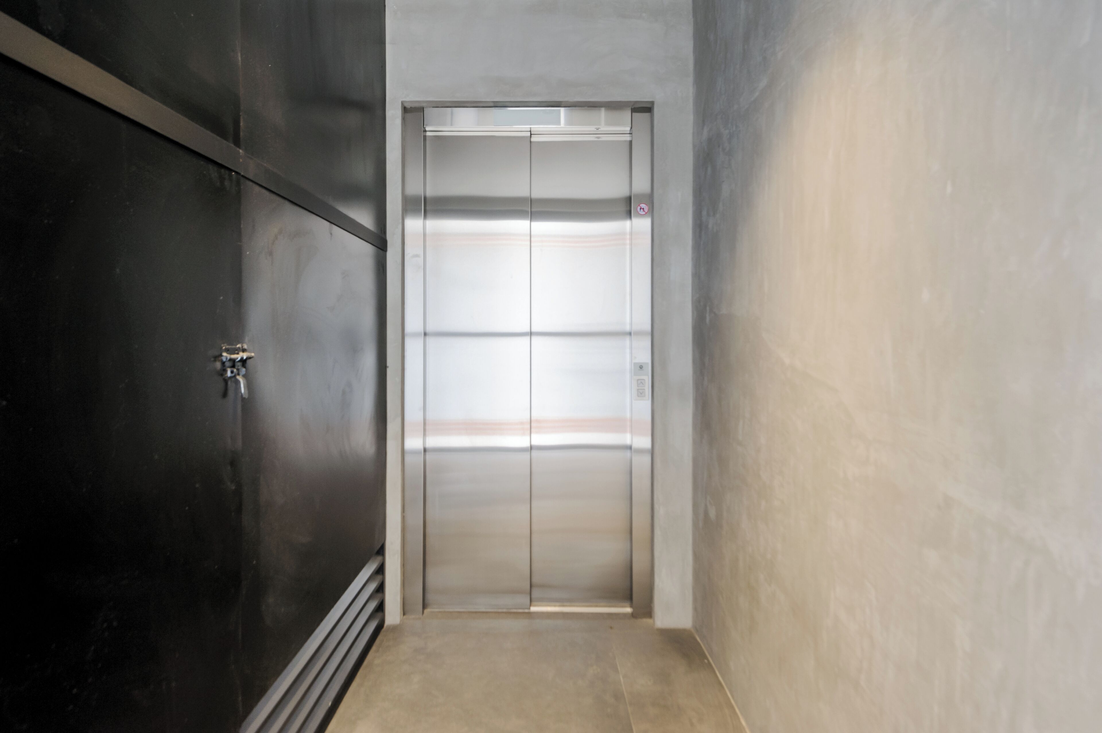 Een moderne lift met een metalen afwerking, een bedieningspaneel en een deur met een veiligheidssymbool.