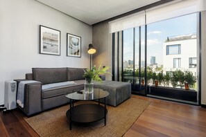 Un salon moderne avec un canapé gris, une table basse en verre et une grande fenêtre donnant sur la ville.
