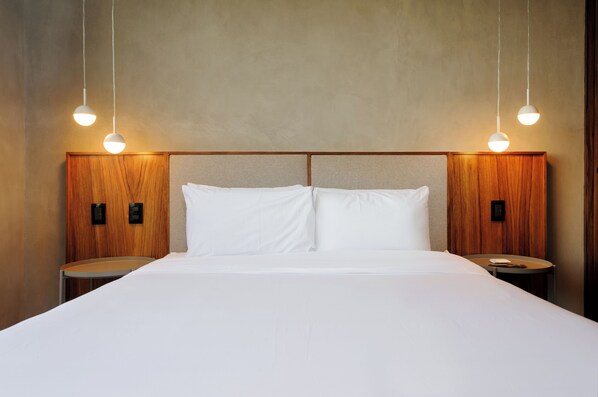 Habitación de hotel con una cama grande, cabecera de madera, dos mesitas de noche e iluminación colgante.