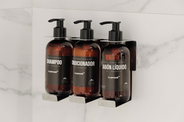 Trois bouteilles de shampoing, d’après-shampoing et de gel douche, posées sur une étagère en marbre blanc.