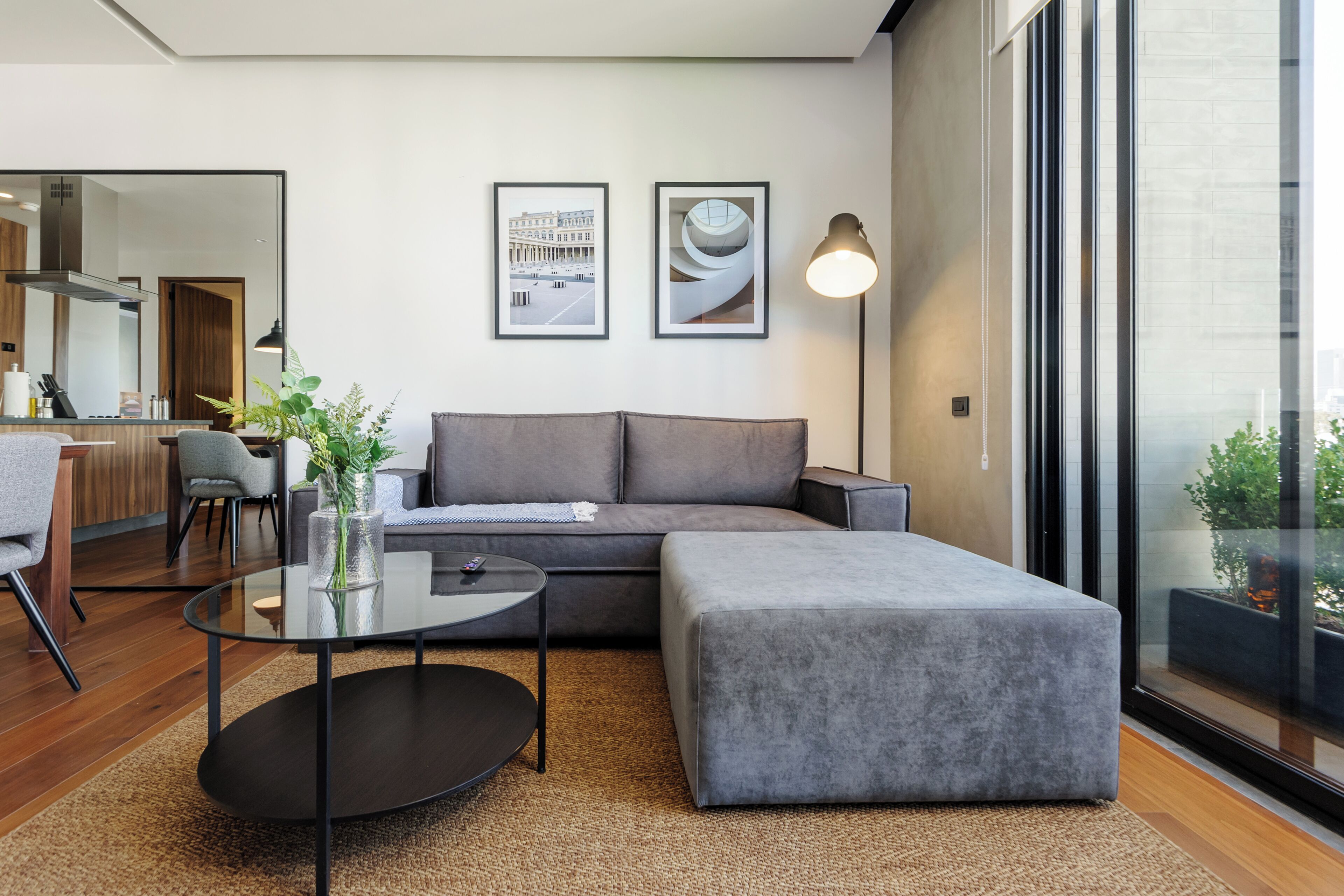 A modern living room with a grey sofa, a glass coffee table, and a large window.
