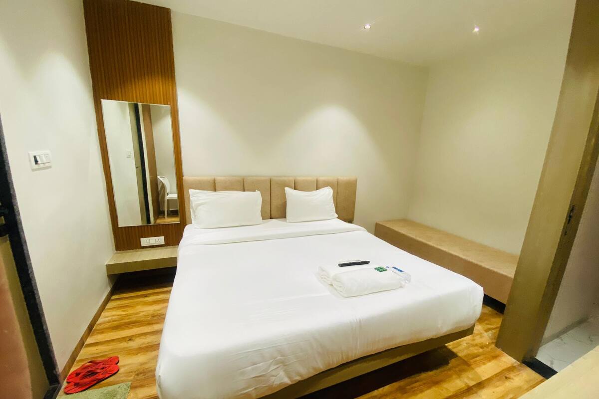 Una habitación de hotel con una cama grande, suelo de madera, una mesita de noche y un espejo.