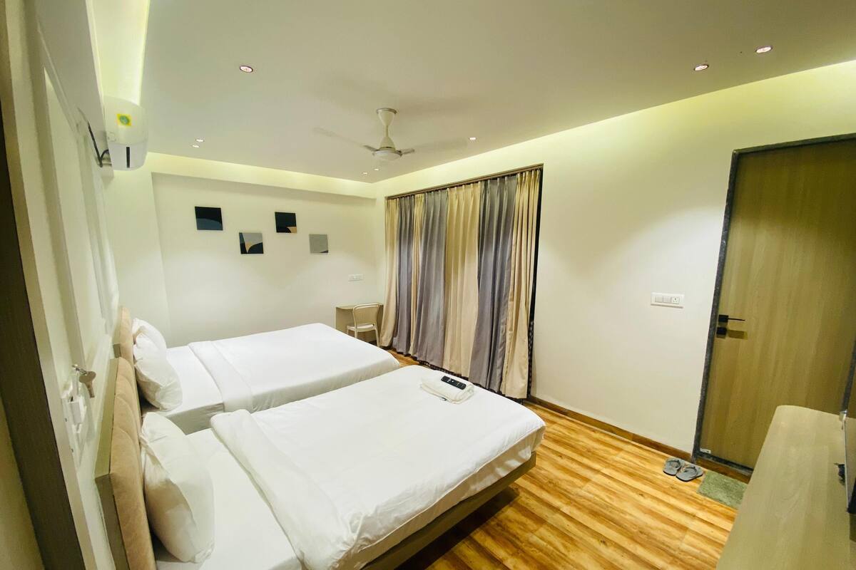 Habitación de hotel con dos camas, un escritorio, una silla, un ventilador de techo y piso de madera.