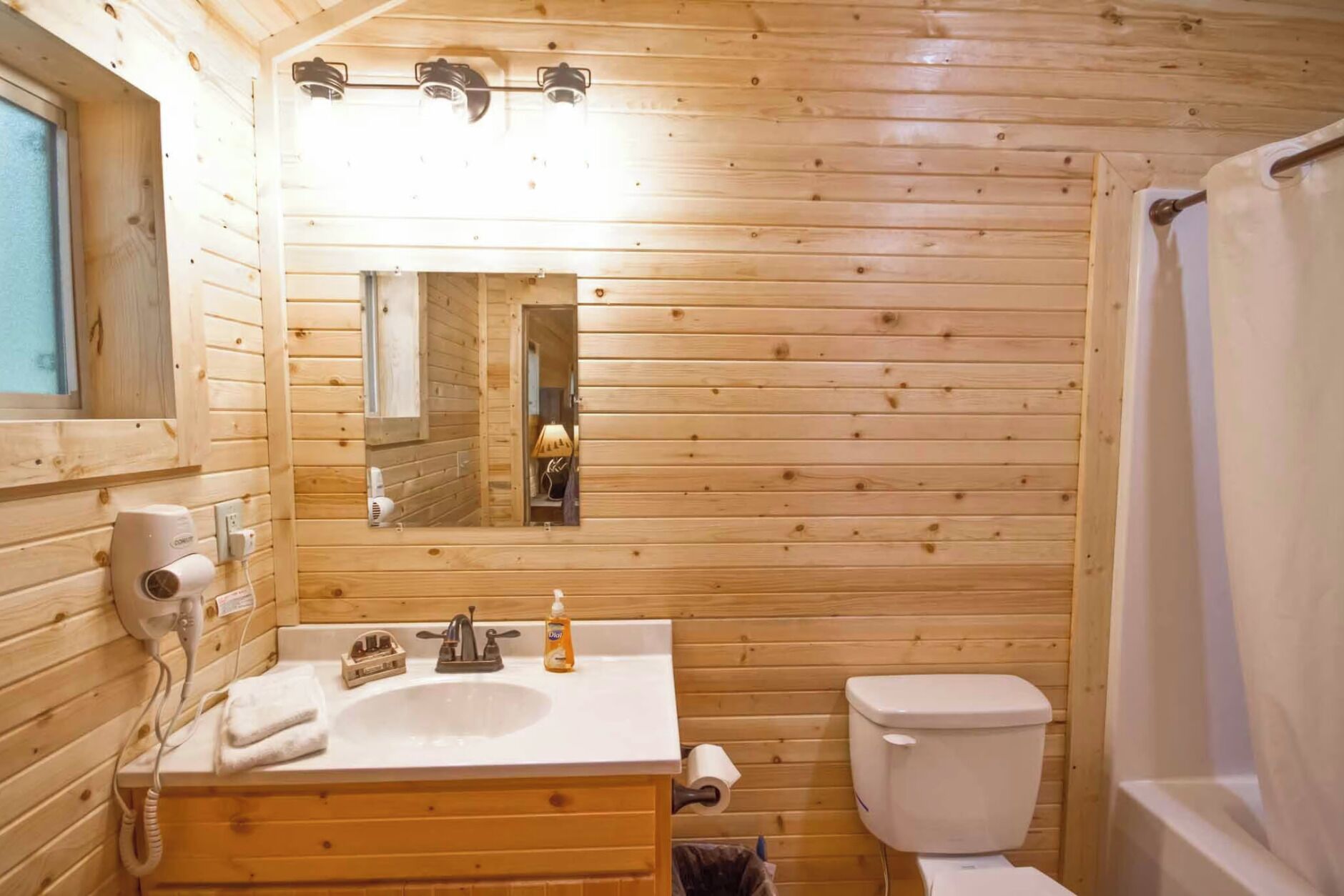 A wooden cabin bathroom with a sink, mirror, toilet, and shower curtain.