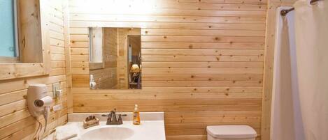 A wooden cabin bathroom with a sink, mirror, toilet, and shower curtain.